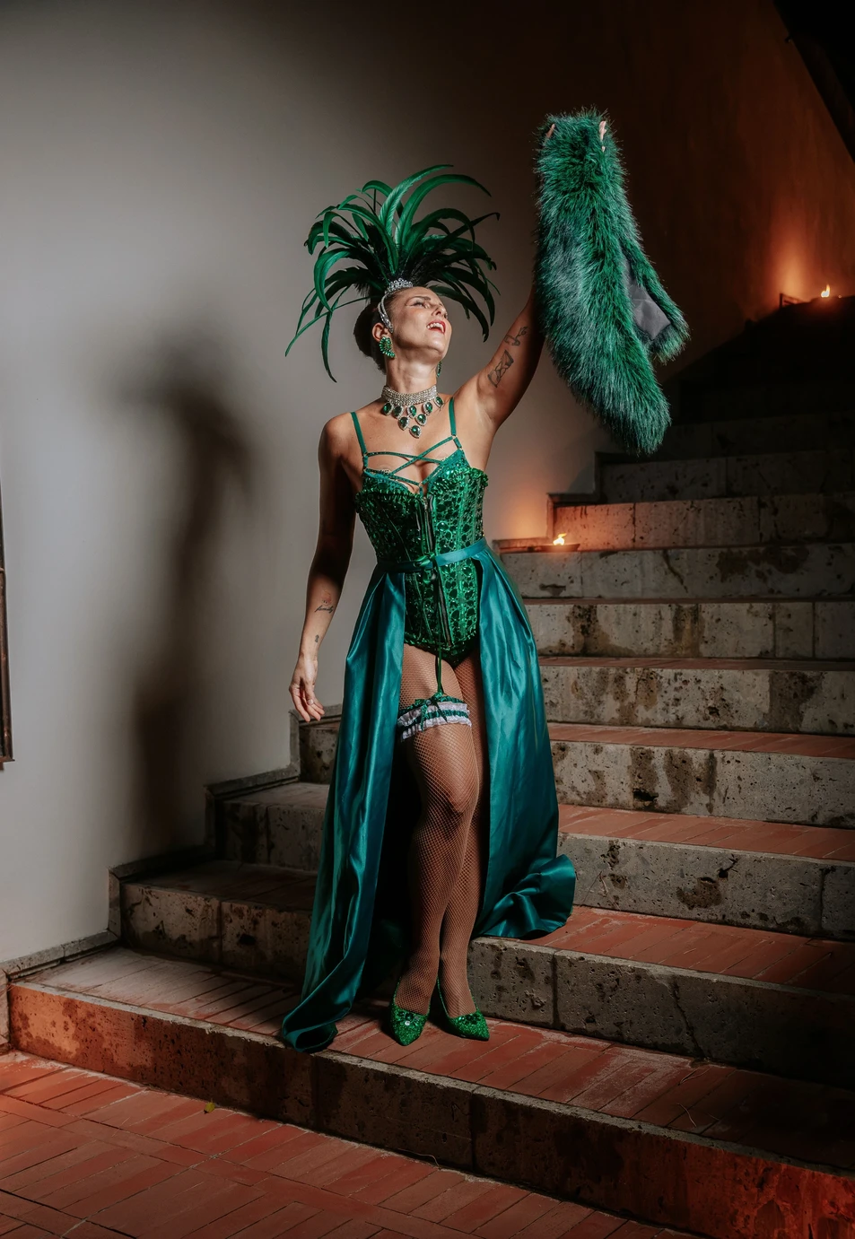 Performer Burlesque in costume verde con piume durante uno spettacolo su una scalinata.