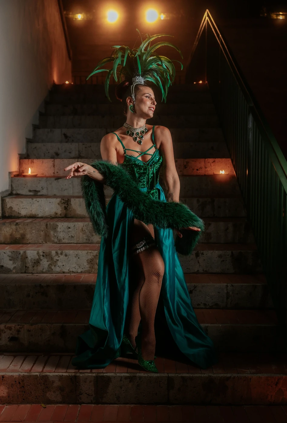 Performer Burlesque in costume verde con piume durante uno spettacolo su una scalinata.