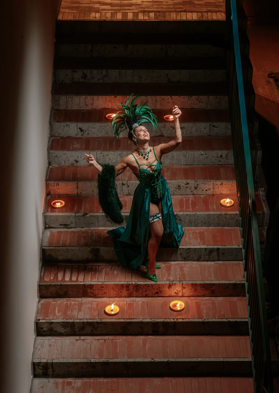 Performer Burlesque in costume verde con piume durante uno spettacolo su una scalinata.