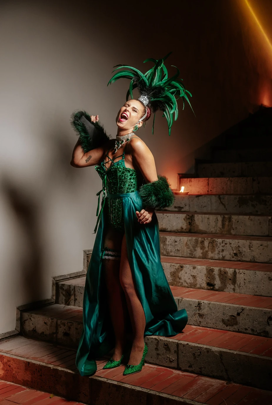 Performer Burlesque in costume verde con piume durante uno spettacolo su una scalinata.
