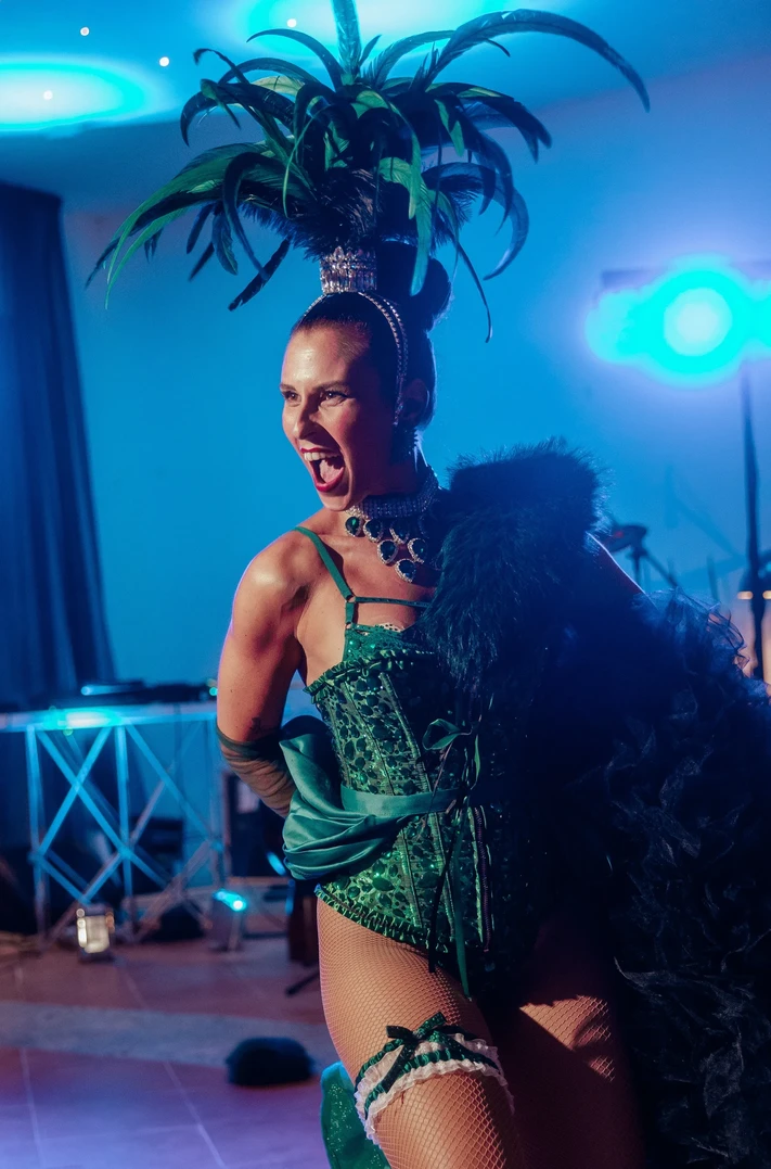 Performer Burlesque con costume di scena e boa di piume sotto luci blu durante uno spettacolo dal vivo.