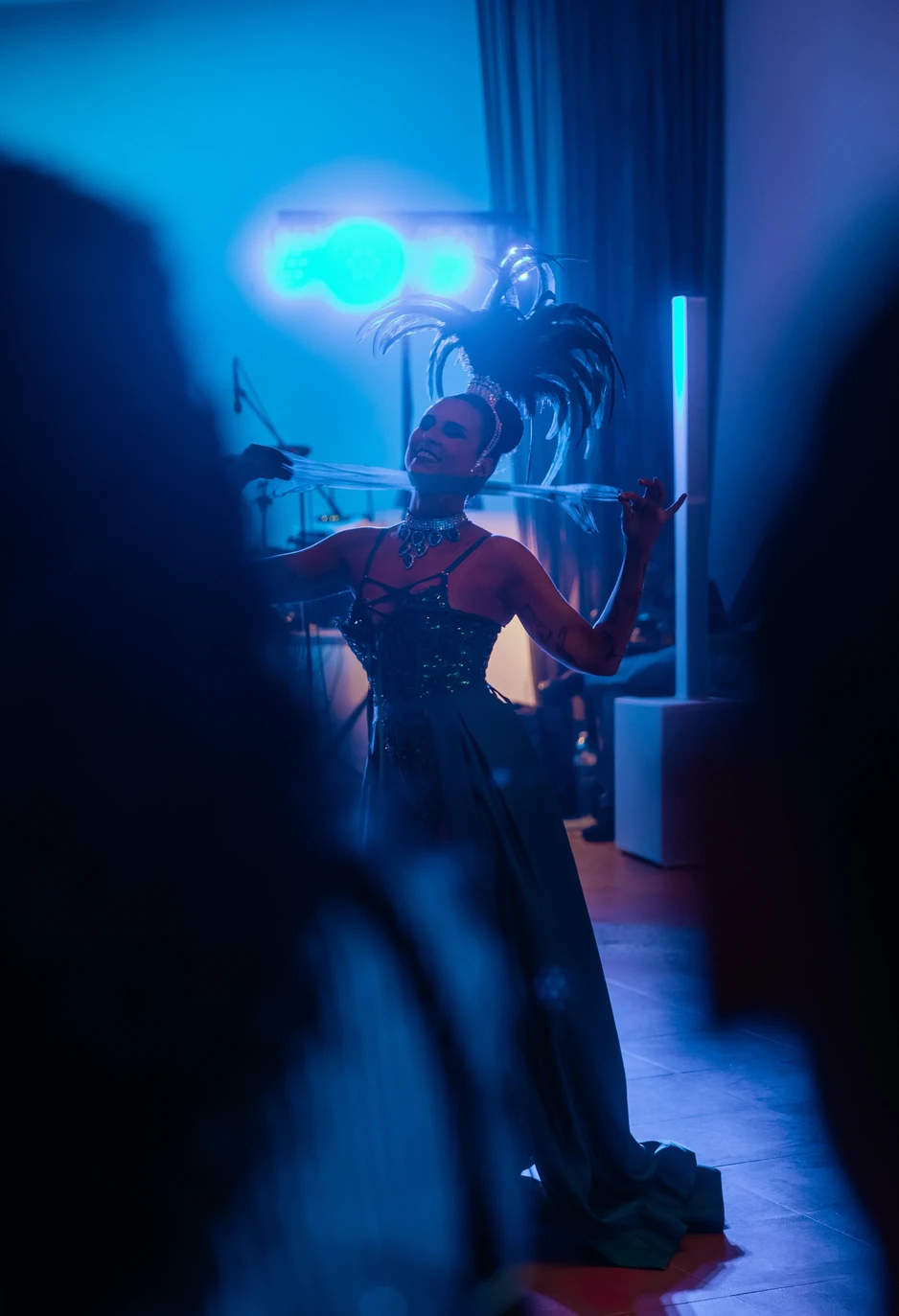 Performer Burlesque con costume di scena e boa di piume sotto luci blu durante uno spettacolo dal vivo.