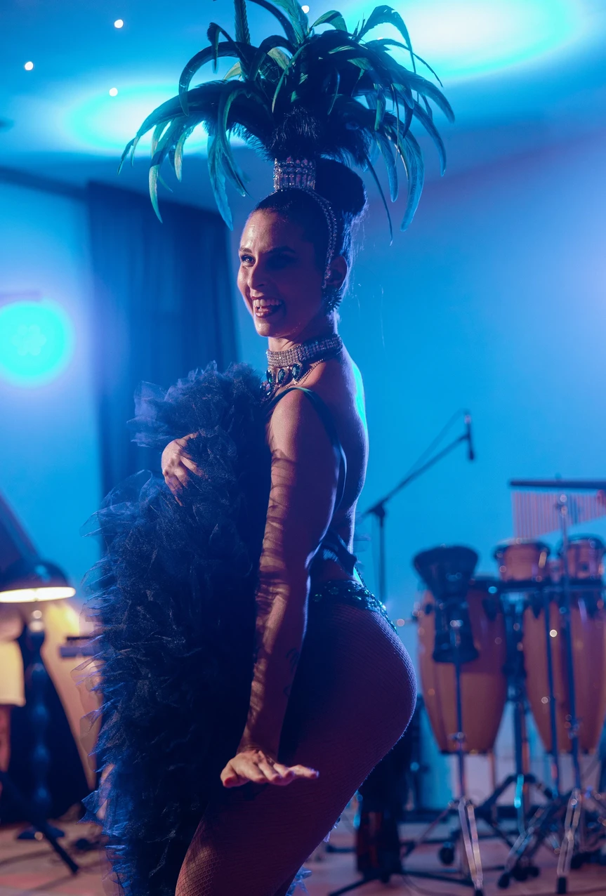 Performer Burlesque con costume di scena e boa di piume sotto luci blu durante uno spettacolo dal vivo.