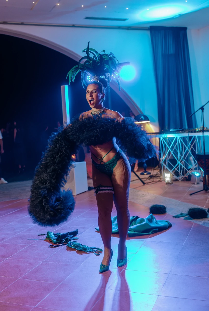 Performer Burlesque con costume di scena e boa di piume sotto luci blu durante uno spettacolo dal vivo.